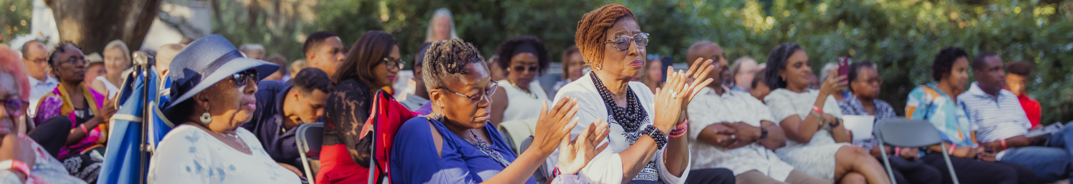 People clapping while seated outside surrounded by oak trees
