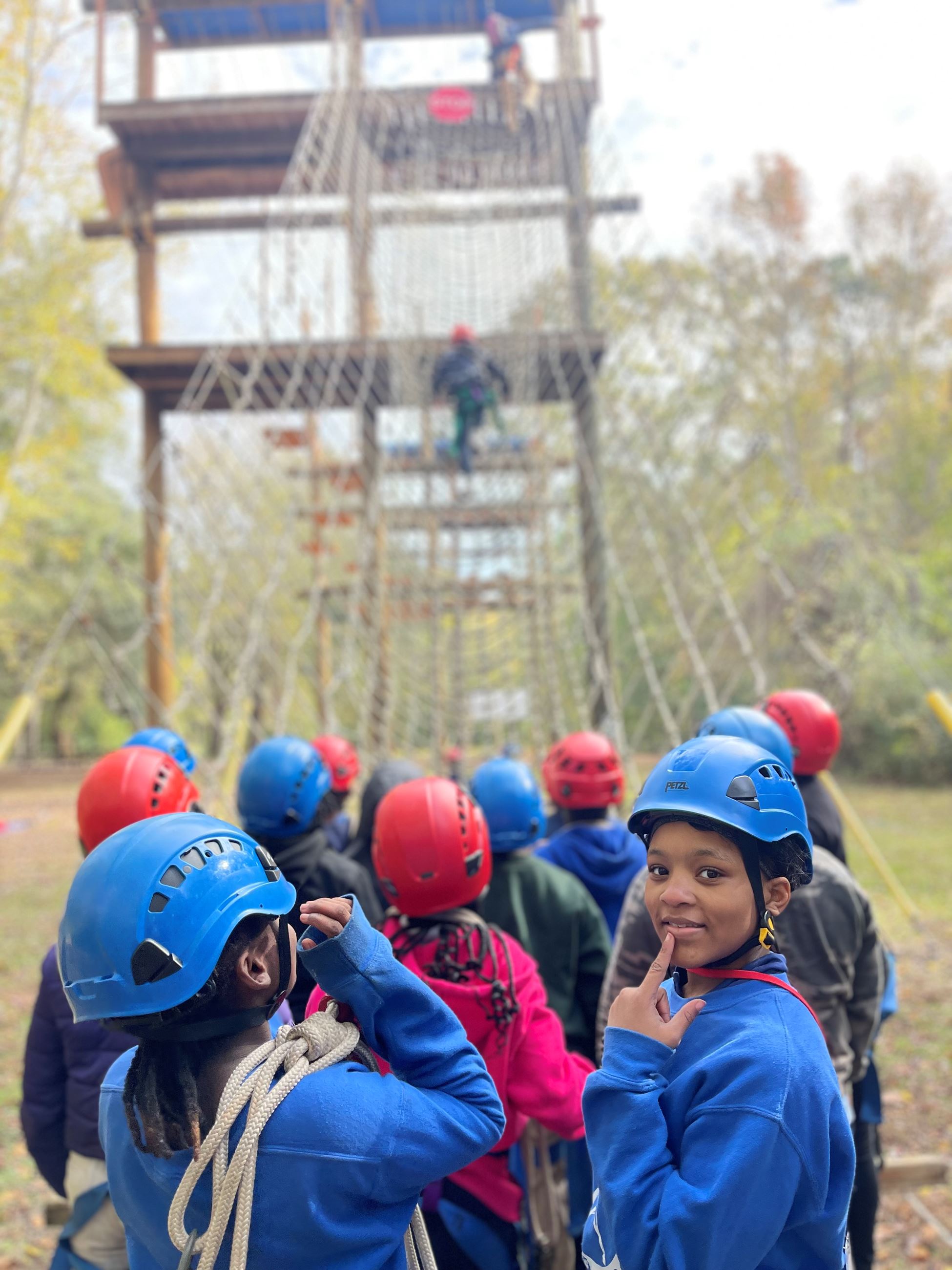 A group of kids wearing helmets look at and prepare to climb up a rope ladder.