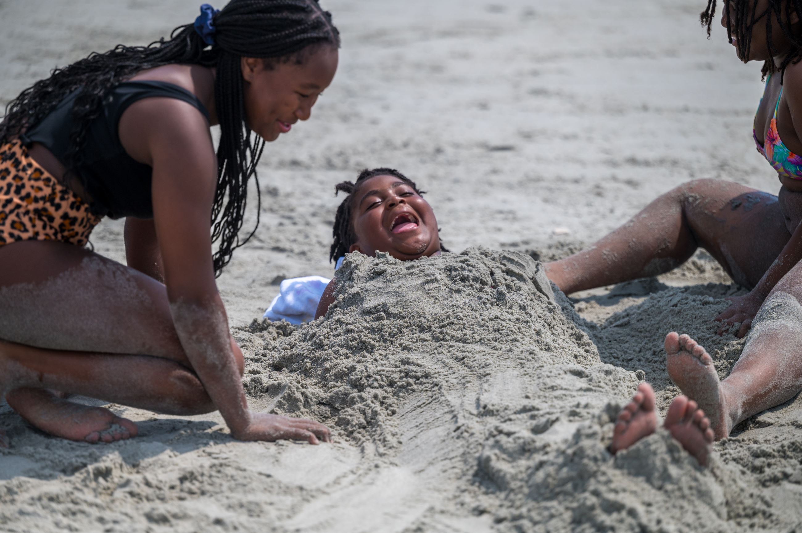 Three kids laughing while playing in the sand at the beach. 