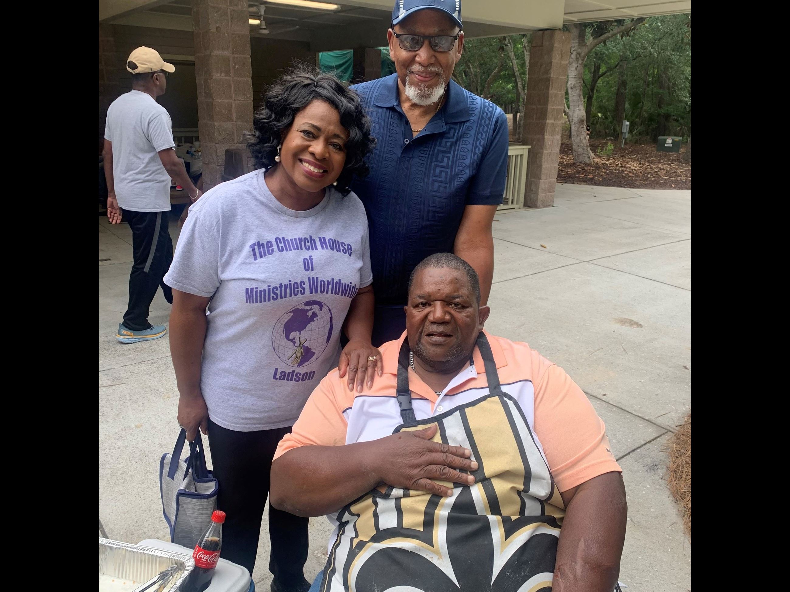 Three people pose for a picture outside near a covered shelter. 