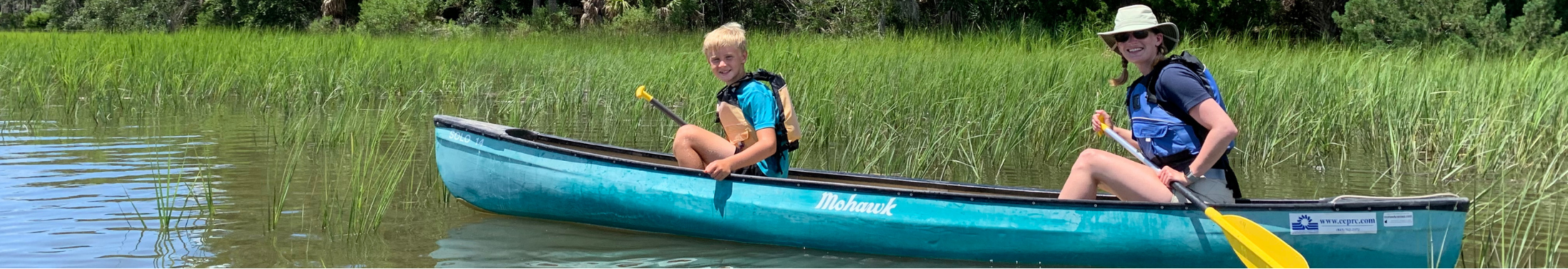 Young boy and camp counselor smiling while paddling a canoe