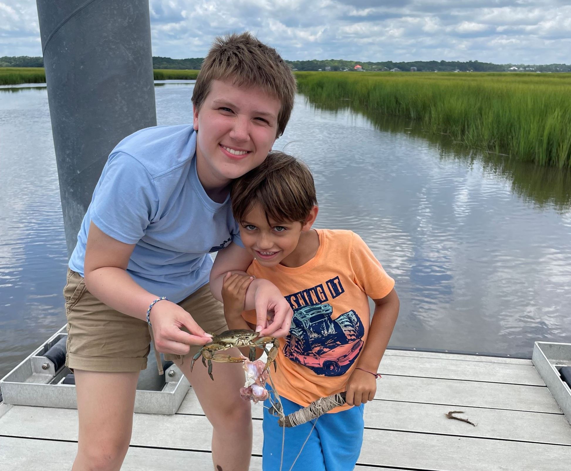 A junior counselor poses with a summer camp participant while on a dock and holding a crab.