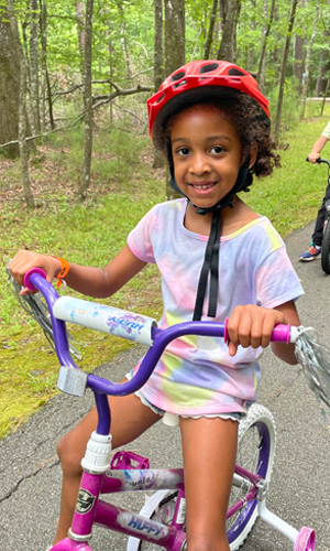 Little girl with a pink helmet riding a bicycle on a trail
